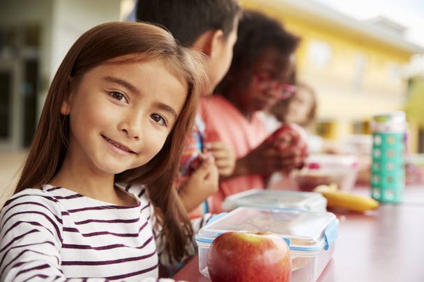 Girl at elementary school lunch table smiling to camera - Φωτογραφία, εικόνα