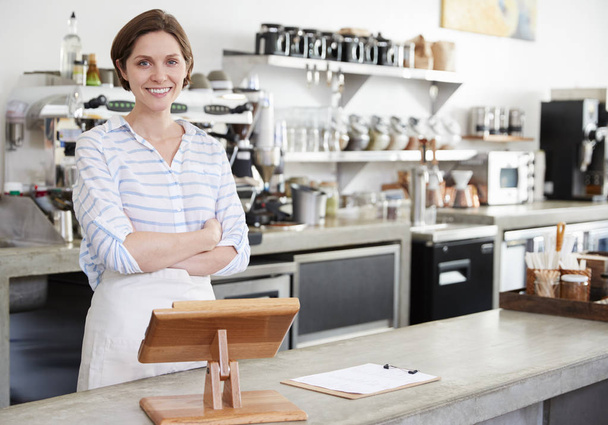 Smiling woman behind counter at coffee shop, arms crossed - Фото, изображение