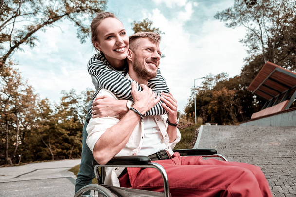 Caring woman gently hugging her disabled boyfriend and looking happy - Fotoğraf, Görsel