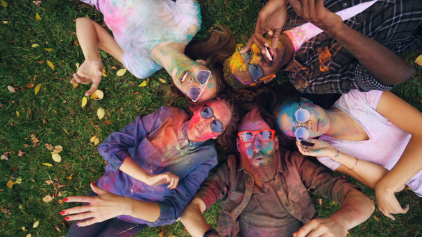 Zeitlupe von oben: verspielte Hipster mit schmutzigen Gesichtern und Klamotten, die auf Gras liegen und auf Camerra schauen und Hände bewegen, die sich entspannen und Natur und Party genießen. - Filmmaterial, Video