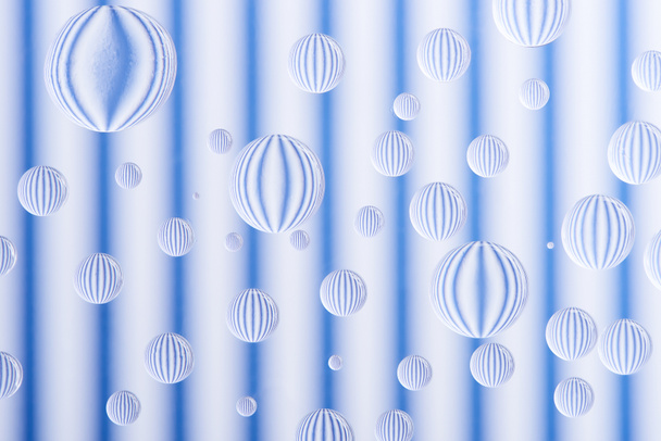 vergrote weergave van transparante waterdruppels op gestreepte achtergrond van wit en blauw - Foto, afbeelding