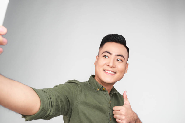 Asian man making selfie with smartphone and showing Ok sign on gray background - Foto, Bild