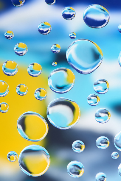 close-up view of beautiful clean water drops on blurred colorful abstract background - Photo, Image