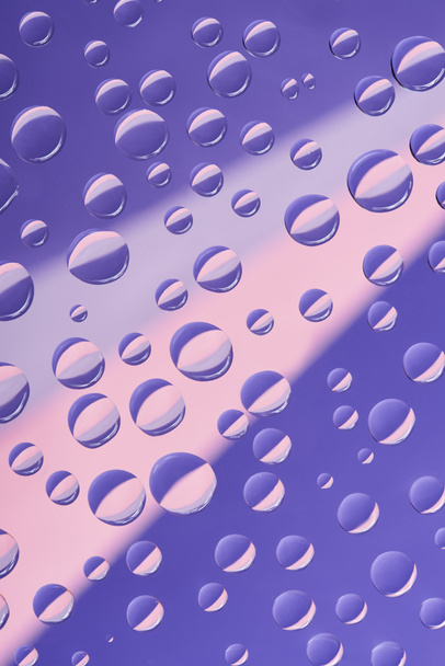 vergrote weergave van transparant water druppels op roze en violet achtergrond - Foto, afbeelding