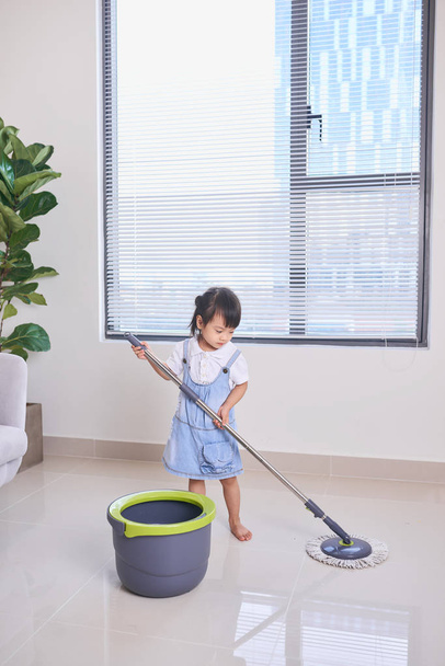 küçük şirin Asyalı kız paspas ile temizlik yapıyor - Fotoğraf, Görsel