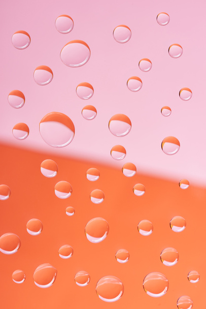 vista de cerca de gotas de agua tranquilas transparentes sobre fondo rosa y naranja
             - Foto, Imagen