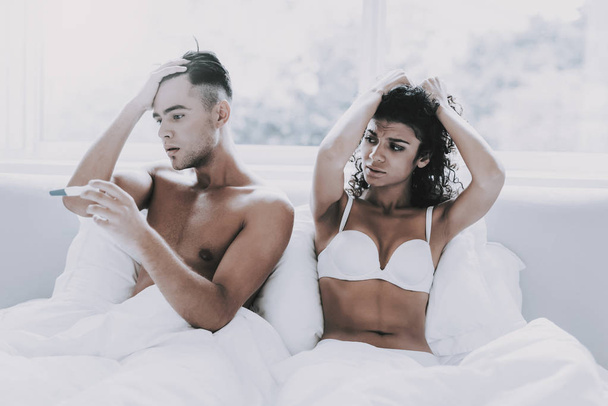 Unhappy Young Couple Looking at Pregnancy Test. Beautiful Sad Woman and Handsome Stressed Man Lying in Bed. Frustrated Young Couple having Problems. Man Depressed because of Result of Pregnancy Test - Foto, Bild