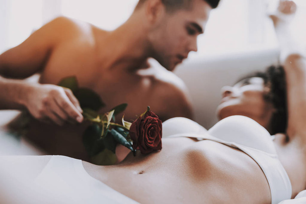 Closeup of Man Caresses Beautiful Woman using Rose. Young Beautiful Couple in Underwear Lying on Bed. Passionate Romantic Lovers about to have Sex at Home. Passion, Intimate Relationship and Love - Photo, Image