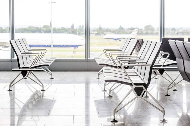 Nykyaikaiset tuolit odotushuoneessa lentokentällä lentokoneella ikkunan takana
 - Valokuva, kuva