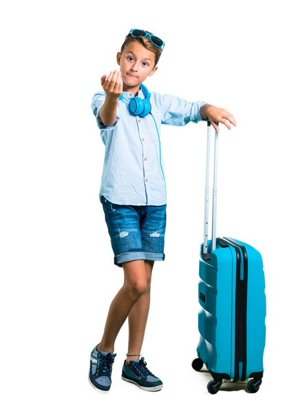 Cuerpo completo de Kid con gafas de sol y auriculares viajando con su maleta presentando y invitando a venir sobre fondo blanco aislado
 - Foto, Imagen