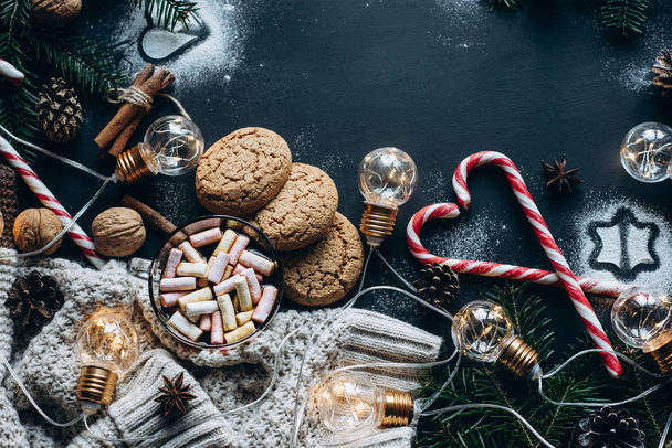 Christmas flat lay. Chocolate or cocoa with marshmallow, cookies, candy and the garland on a dark background. - Фото, зображення