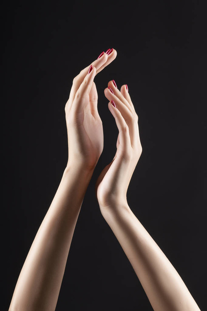 Closeup of beautiful woman hands with red manicure on the nails. Cream for palms, manicure and beauty treatment. Elegant and graceful arms with slender graceful fingers. Copy space. Isolated on black. - Photo, image