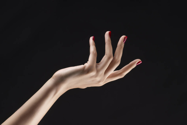Closeup of beautiful woman hand with red manicure on the nails. Cream for palms, manicure and beauty treatment. Elegant and graceful arm with slender graceful fingers. Copy space. Isolated on black. - Photo, image