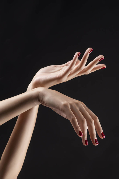 Closeup of beautiful woman hands with red manicure on the nails. Cream for palms, manicure and beauty treatment. Elegant and graceful arms with slender graceful fingers. Copy space. Isolated on black. - Foto, imagen