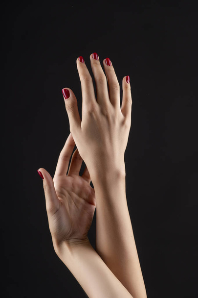 Closeup of beautiful woman hands with red manicure on the nails. Cream for palms, manicure and beauty treatment. Elegant and graceful arms with slender graceful fingers. Copy space. Isolated on black. - Photo, image
