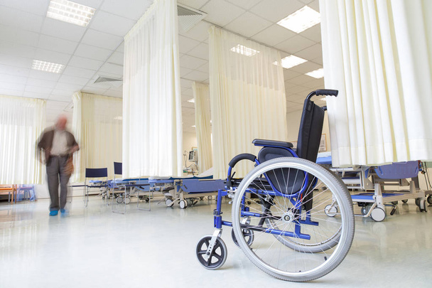 A wheelchair in modern hospital with empty beds and a blurred patients figure. - Foto, afbeelding