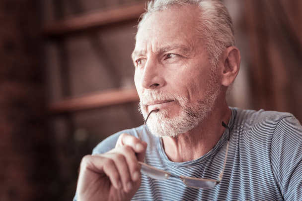 Homem idoso segurando seus óculos e olhando para longe
 - Foto, Imagem