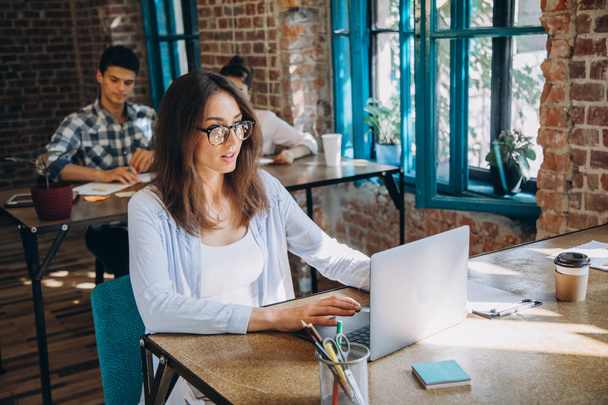 Молода бородата бізнес-леді в джинсовій сорочці сидить за столом і використовує ноутбук з графіками, графіками і діаграмами на екрані. Чоловік працює.startu
 - Фото, зображення