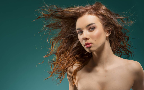 portrait of sensual young girl with brown wavy flying hair and pretty make-up looking in camera with naked shoulders on green - Foto, Imagen