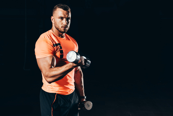 handsome fit sportsman working out with barbells in dark gym - Zdjęcie, obraz