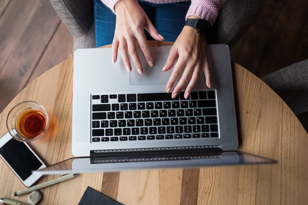 Женщина работает с помощью ноутбука на деревянном столе. Руки печатают на клавиатуре
. - Фото, изображение
