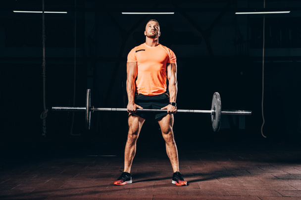 handsome athletic man working out with barbell in dark gym and looking up - 写真・画像