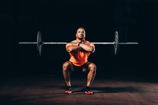 bel homme musclé faisant squats avec haltère dans la salle de gym sombre
 - Photo, image