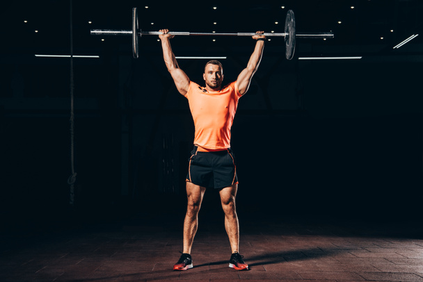 handsome muscular man working out with barbell in dark gym - Fotoğraf, Görsel
