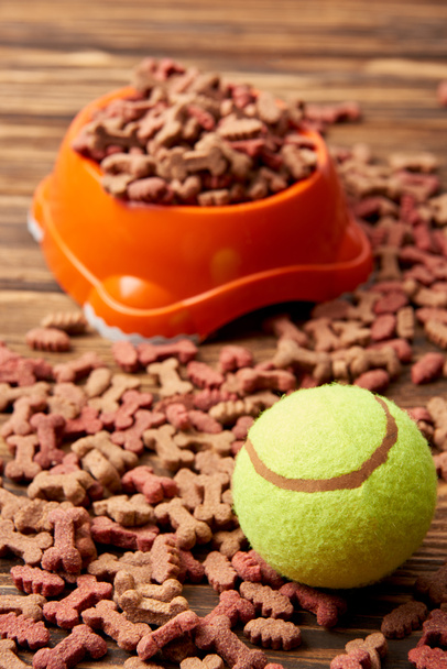 κλείνω πάνω θέα από πλαστικό μπολ με τρόφιμα σκυλιών και μπάλα στο ξύλινο τραπέζι - Φωτογραφία, εικόνα