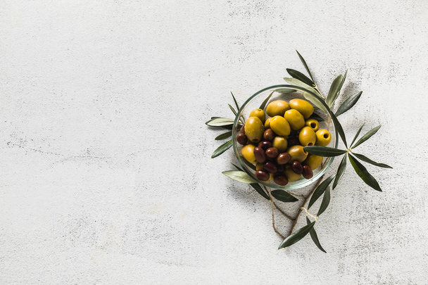 Assortiment olijven in een transparante kom en een tak van de olijfboom. snack of voorgerecht. hors d'oeuvre - Foto, afbeelding
