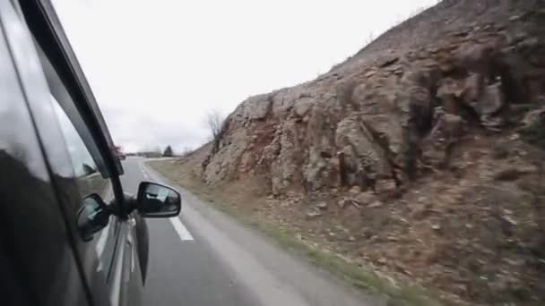 Een auto gaan op een bochtige weg in de buurt van de heuvels. Reflectie van jonge vrouwelijke passagier in vleugel spiegel. - Video