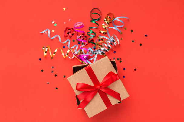 Gift box with colourful streamers on red background - Photo, Image