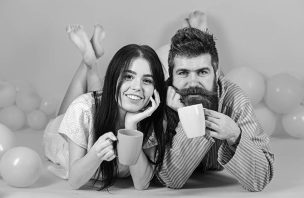 Couple relax in morning with coffee. Couple in love drink coffee in bed. Man and woman on smiling faces lay, pink background. Weekend morning concept. Man and woman in domestic clothes, pajamas. - Foto, Imagem