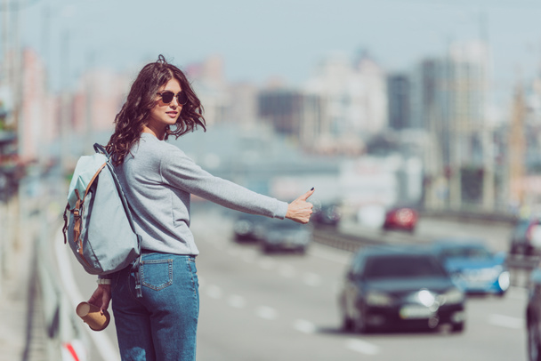 young woman with backpack and coffee to go hitchhiking at road - Photo, Image