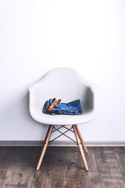 Designer plastic chair on a white wall background. Blue jeans on a chair. Object in the interior - Фото, изображение