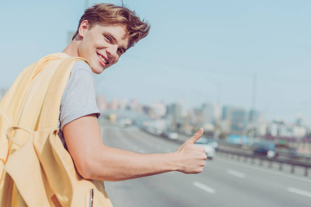 smiling young man hitchhiking on road - Photo, Image