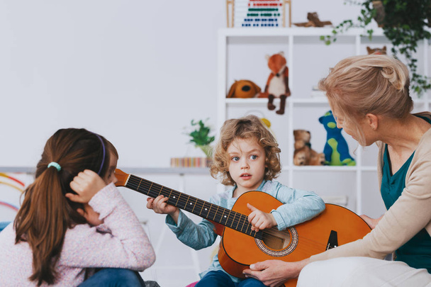 Cute little boy learning how to play guitar during lesson in preschool, photo with copy space - Valokuva, kuva