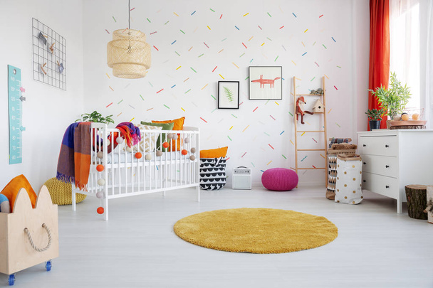 Orange round rug and posters in colorful kid's room interior with cradle and wooden crate. Real photo - Photo, image