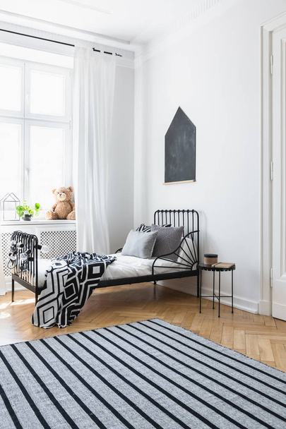 Striped carpet in white bedroom interior with patterned blanket on bed near window. Real photo - Fotoğraf, Görsel