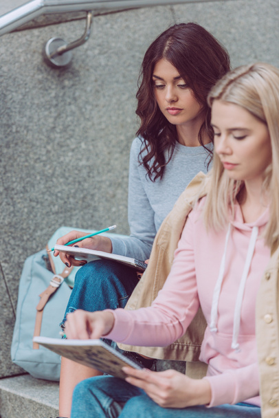 young women with notebooks resting on city steps during journey - Foto, Bild