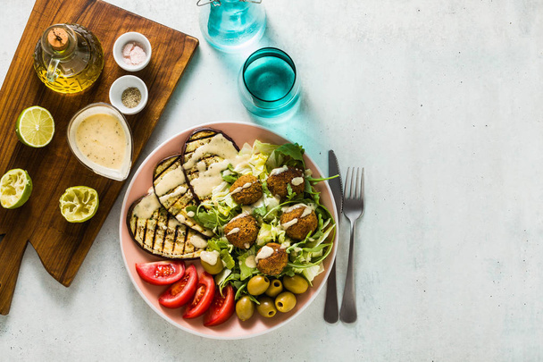 an appetizing dinner or lunch from a salad with tomatoes, grilled eggplants and legume falafel with sesame tahini dressing. Vegan healthy food for the whole family - Photo, Image