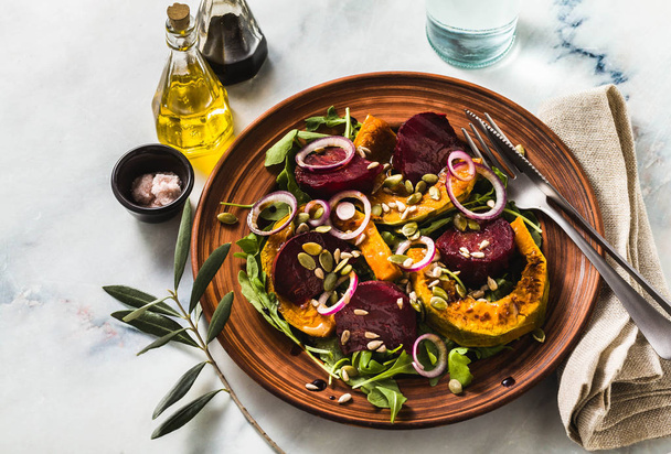 warm salad of baked pumpkin and beets with arugula and seeds on a marble table. healthy vegan cuisine for the whole family - Foto, Imagen