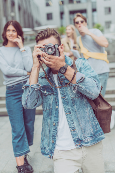 selective focus of tourist taking picture on photo camera with friends behind on street - Фото, изображение