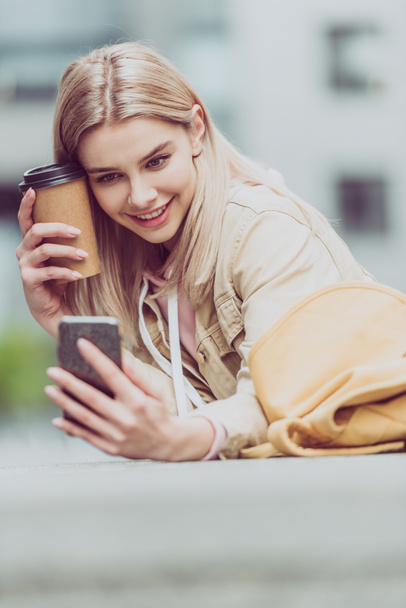 cheerful blonde girl with coffee to go taking selfie on smartphone - Фото, зображення