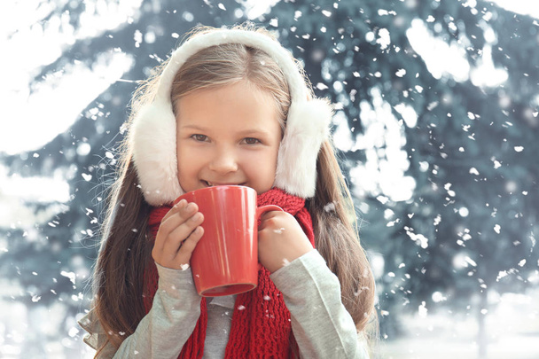 Το χαριτωμένο μικρό κορίτσι σε ζεστά ρούχα και με φλυτζάνι της καυτής σοκολάτας στη χιονισμένη μέρα - Φωτογραφία, εικόνα