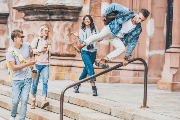 young stylish friends walking in city while man jumping over railing - 写真・画像
