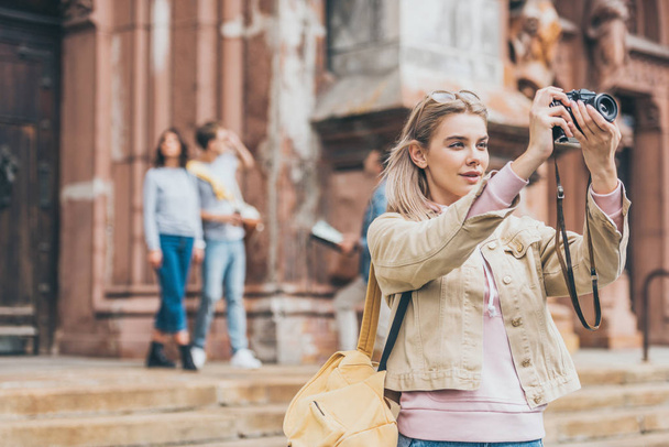 young woman taking photo of city on camera with friends behind - Фото, зображення