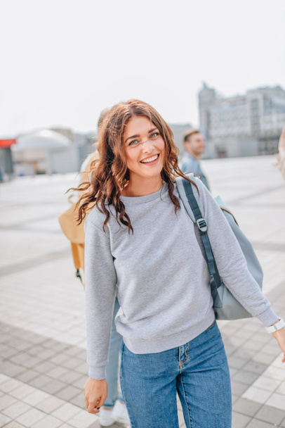 attractive cheerful girl laughing and walking with backpack in urban city - Zdjęcie, obraz
