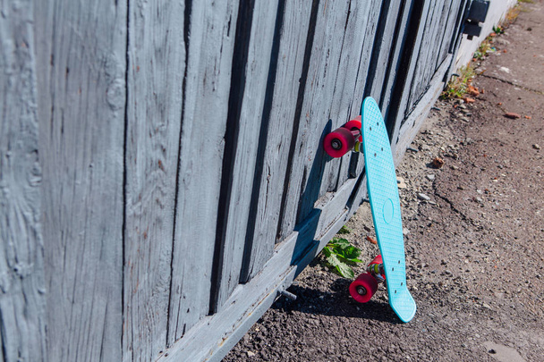 Blue plastic skateboard penny board with pink wheels stands next to the wall. - Фото, изображение