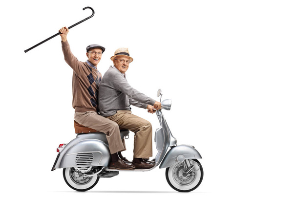 Full length shot of two senior men on a vintage scooter, one holding a cane up isolated on white background - Foto, imagen